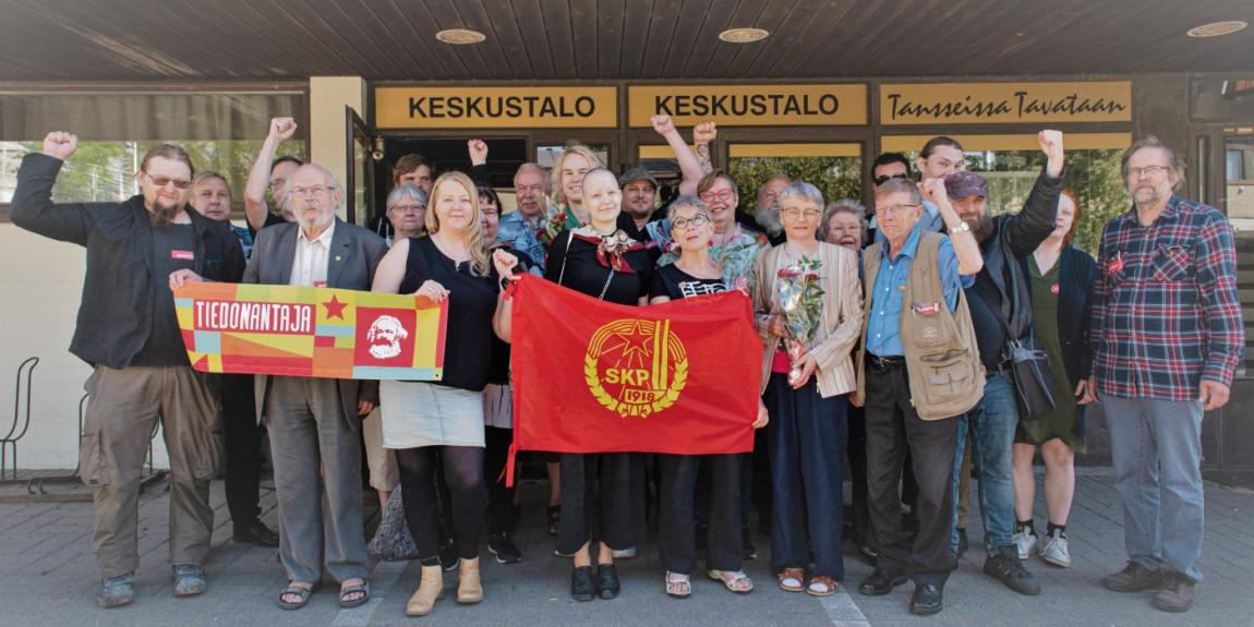 SKP:n tovereita seisoo iloisina puolueen lipun takana.