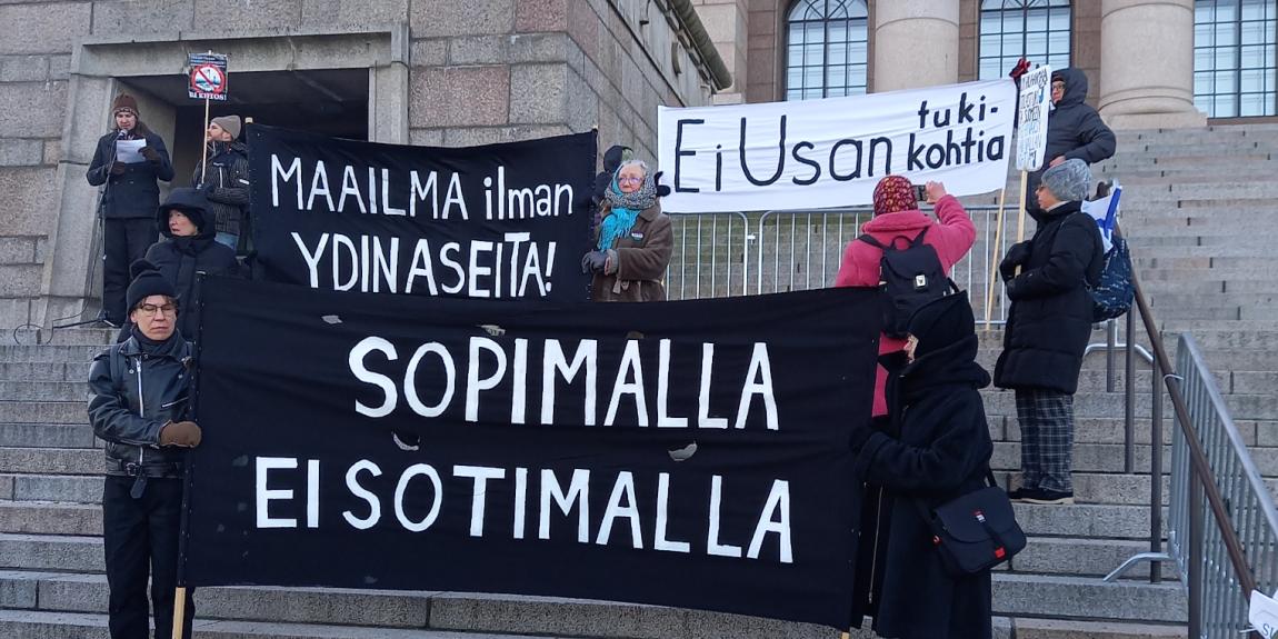 Ihmisiä banderollien kanssa Eduskuntatalon portailla. "Ei USA:n tukikohtia", Maailma ydinaseita, Sopimalla ei sotimalla.