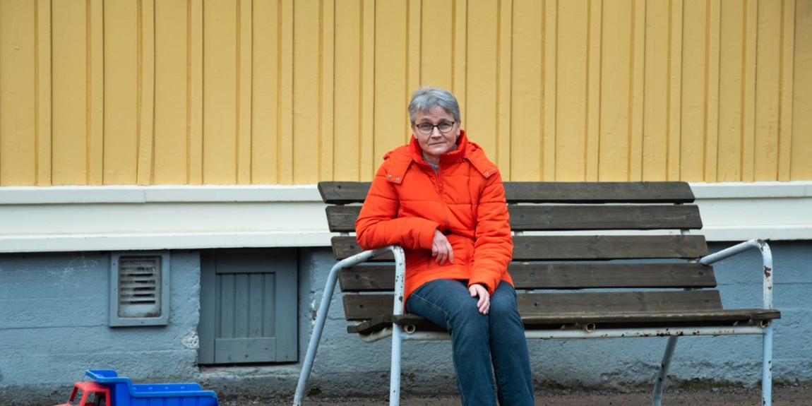 Mervi Grönfors istuu penkillä, jaloissa on lasten leikkikuorma-auto.