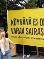 Amnesty Internationalin ihmiset pitävät isoa keltaista banderollia, jossa lukee "Köyhänä ei ole varaa sairastaa."