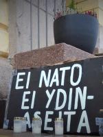 Kyltti, jossa lukee "Ei Nato, Ei ydinaseita" ja hautakynttilöitä.