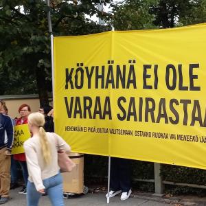 Amnestyn iso keltaine banderolli, jossa lukee "Köyhänä ei ole varaa sairastaa."