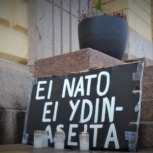 Kyltti, jossa lukee "Ei Nato, Ei ydinaseita" ja hautakynttilöitä.