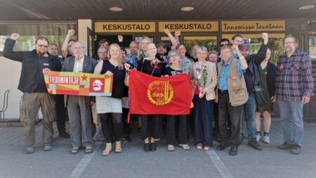 SKP:n tovereita seisoo iloisina puolueen lipun takana.