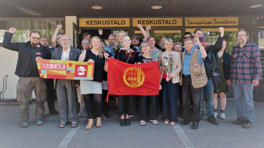 SKP:n tovereita seisoo iloisina puolueen lipun takana.