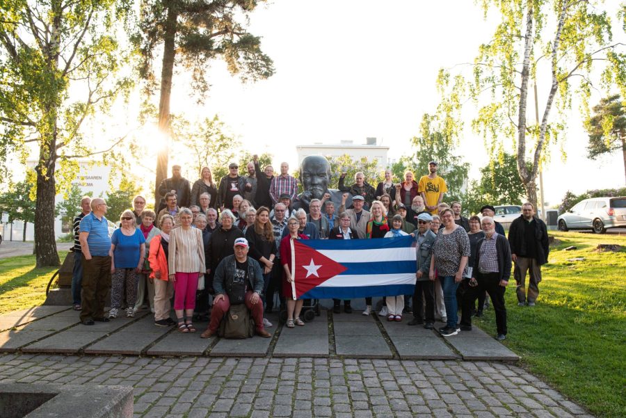 Osallistujia yhteiskuvassa Kuuban suurlähettilään kanssa Kotkan Lenin-patsaan edustalla ulkona kesällä 2022.