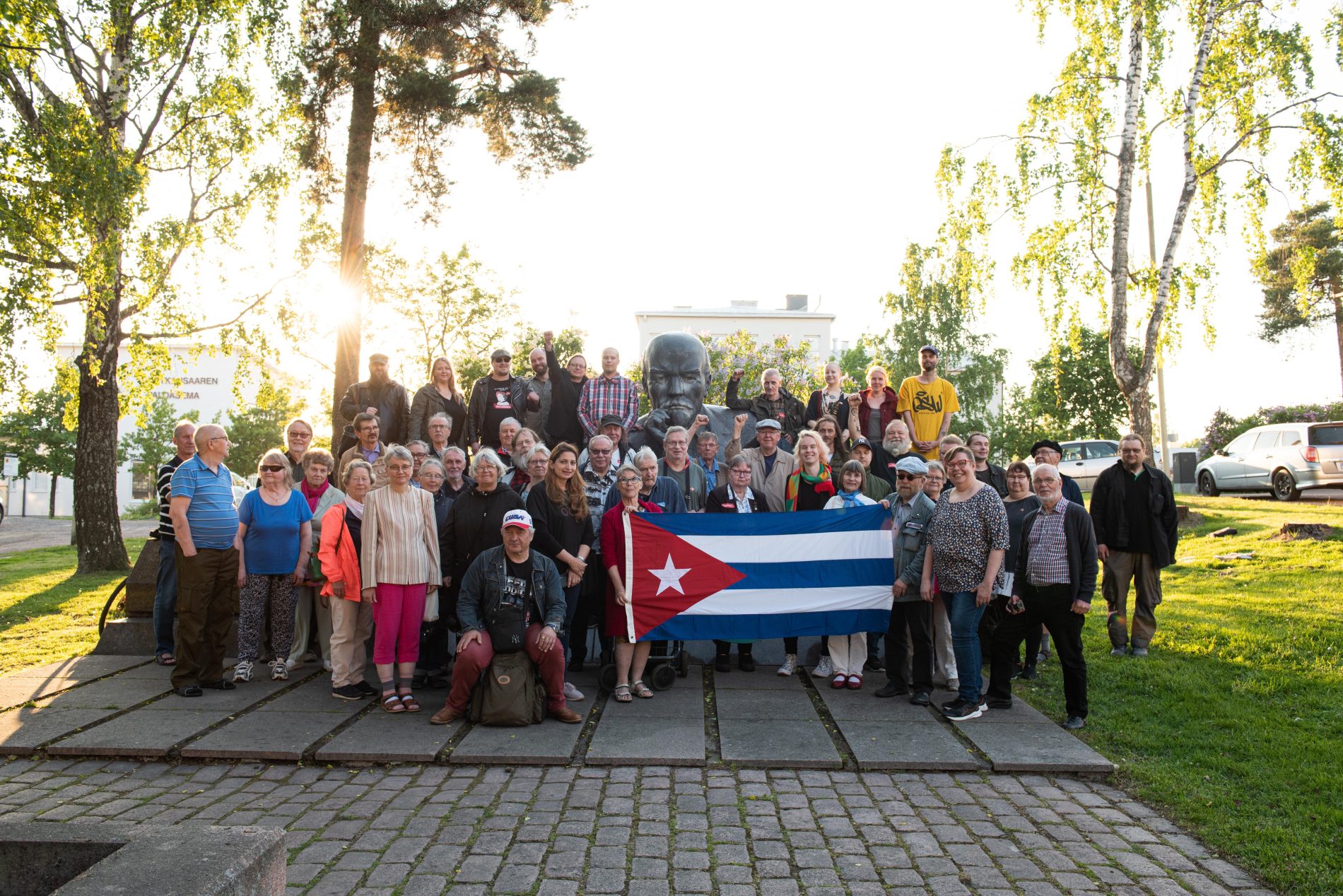 Osallistujia yhteiskuvassa Kuuban suurlähettilään kanssa Kotkan Lenin-patsaan edustalla ulkona kesällä 2022.