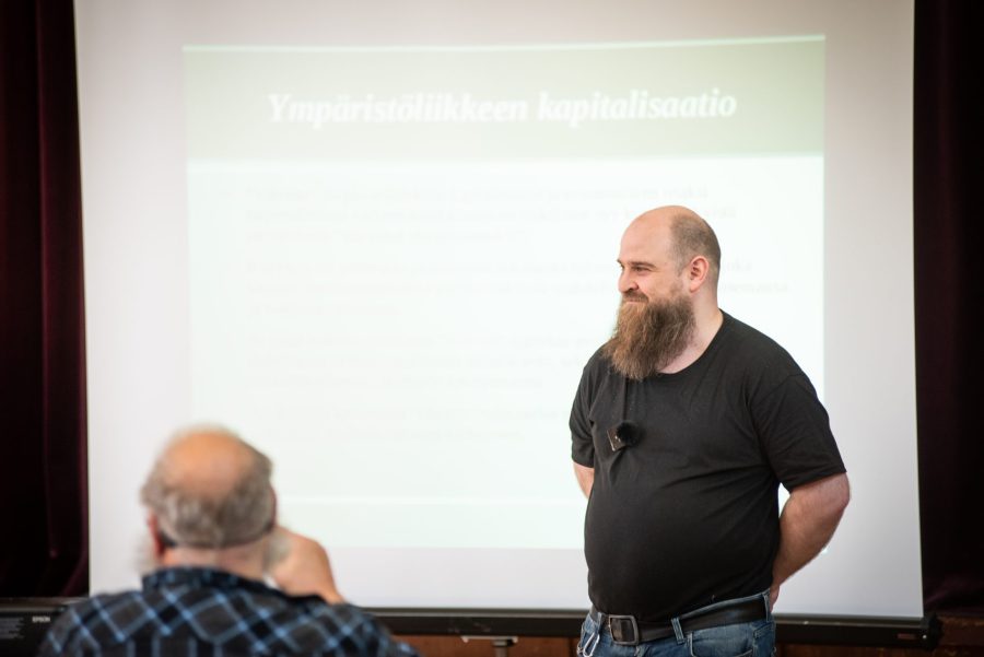 Jari Karttunen esitelmöimässä tapahtumassa, taustalla valkokangas.
